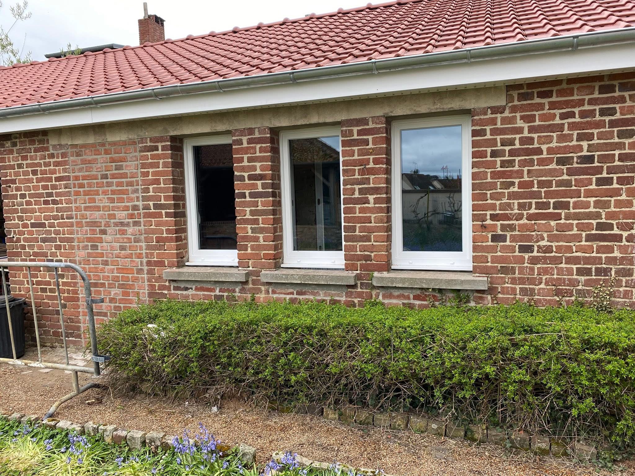 Série de trois fenêtres PVC blanches sur mur en briques
